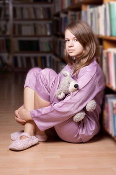 The girl in pink pajamas in the library among the books
