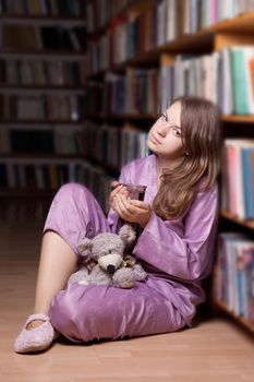 The girl in pink pajamas in the library among the books