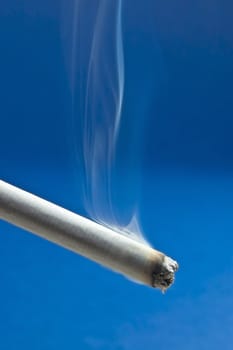 Burning cigarette with smoke on blue background 