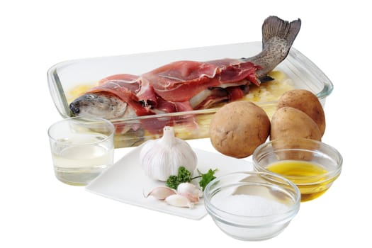 fresh trout with slices of ham on a layer potatoes and all the ingredients necessary for its preparation to the oven