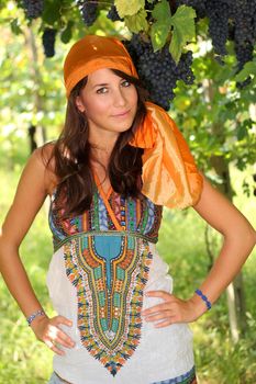 Beautiful girl dressed like gypsy posing in green vineyard with grapes 