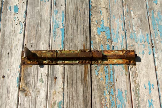 A rusty vintage bolt, sliding lock, screwed to a pair of sun bleached wooden doors with flaking blue paint.