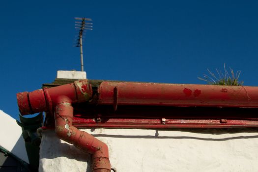 A broken section of plastic guttering and downpipe joint painted red on a red facia.