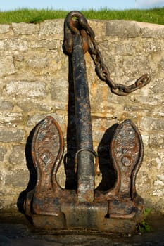 A vintage ship's anchor, rusted with black paint and chain, on display against a stone wall.