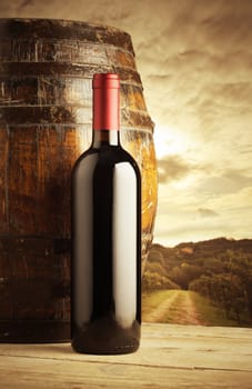 red wine bottle and wodden barrel, vineyard on background