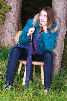 Young woman with umbrella in very fashionable clothes sitting in the forest