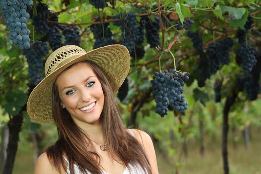 Beautiful country girl with blue eyes smiling. Grapes and vineyard as background
