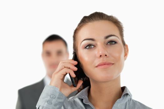 Close up of confident businesswoman on the phone with colleague behind her against a white background