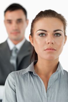 Close up of serious looking businesswoman with colleague behind her against a white background