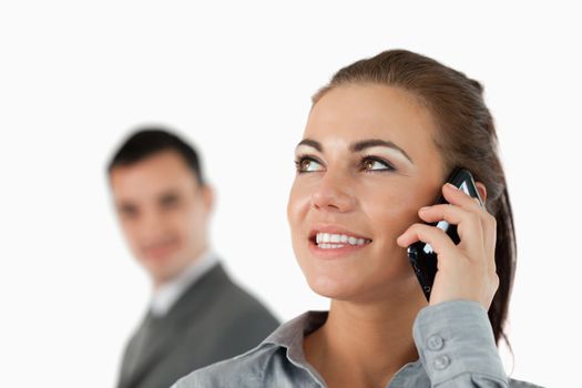 Close up of smiling businesswoman on the phone with colleague behind her against a white background