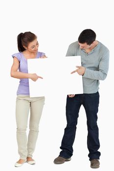 Young couple pointing at sign they are holding together against a white background