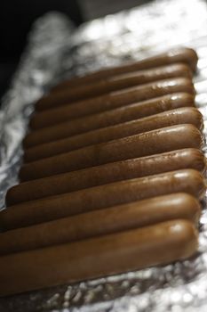 Row of tasty brown sausages being grilled on tinfoil with shallow dof