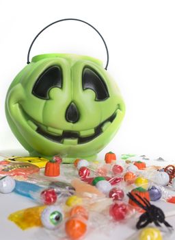 Green pumpkin halloween bucket filled with candy, candy corn, suckers, and cookies.  Isolated on white background