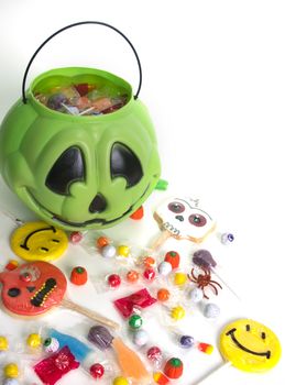 Green pumpkin halloween bucket filled with candy, candy corn, suckers, and cookies.  Isolated on white background