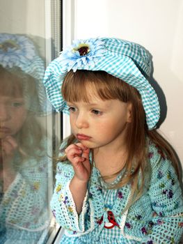 Cute thoughtful  little girl in blue dress looking through the window