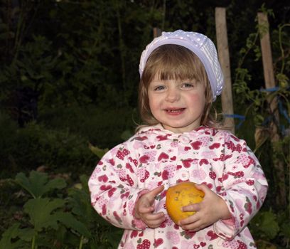 Cute smiling little girl with pumkin on evening garden background