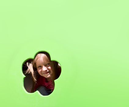 Cute smiling little girl looking through the hole on green background