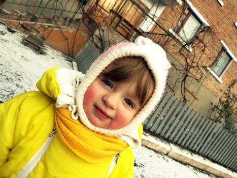 Funny little girl in warm clothes on winter house background