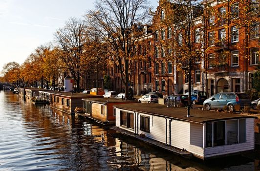 Image of a canal with specific floating houses in Amsterdam during an autumn afternoon.