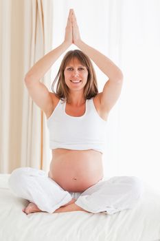 Attractive pregnant female doing yoga on a bed in her apartment