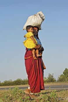 Female farm worker making her way home with babe in arms, baggage carried on her head, in bare feet in the hinterlands of maharashtra, India wearing ankle bracelets. September 29th, 2012, editorial