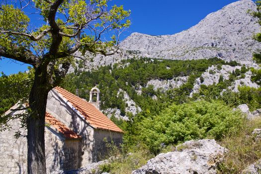 Old stone chapel near village of Tucepi below towering mountains of Biakovo nature park on Makarska Riviera in Dalmatia, Croatia