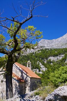 Old stone chapel near village of Tucepi below towering mountains of Biakovo nature park on Makarska Riviera in Dalmatia, Croatia