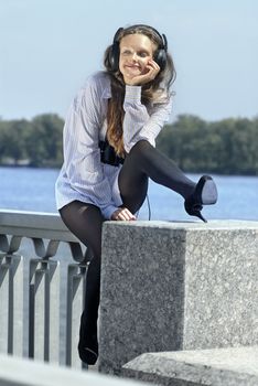 Happy girl listening music on quay near the river