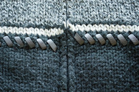 Closeup of wool knit sweater texture decorated with leather stitch. White grey and black colors background