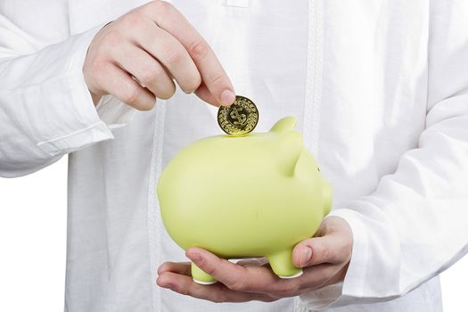 Close-up photograph of a man putting a coin in a green piggy bank.