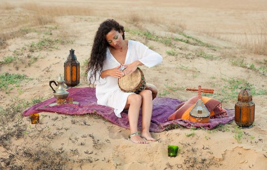 Woman playing a traditional djembe in a desert setting