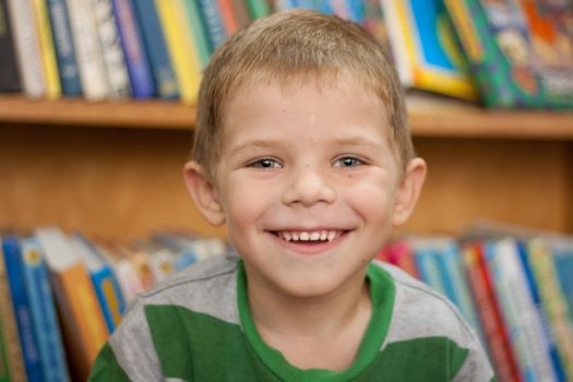 small boy smiling on the background of the books in the library