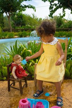 Small girl giving her old doll a cup of tea