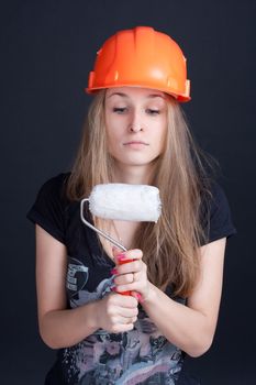 The girl in the construction helmet with a roller in his hand against a dark background