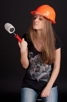 The girl in the construction helmet with a roller in his hand against a dark background