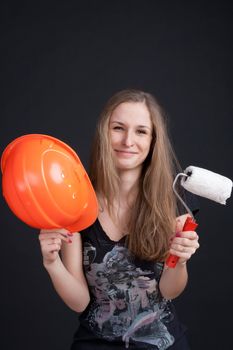 The girl in the construction helmet with a roller in his hand against a dark background