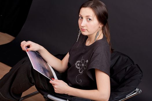 A serious girl sitting on a chair and looks into the camera studio photography