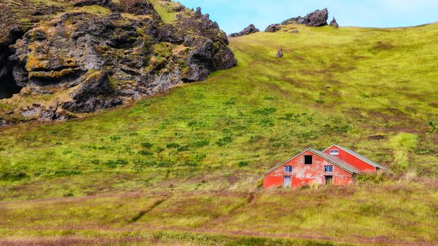 Old wooden red abandoned barn in green grass meadow, Iceland