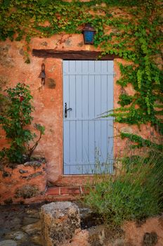 Old blue entrance door in orange wall, Provence, France