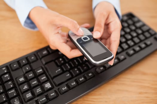 Businesswoman holding a mobile phone above a keyboard in an office