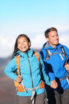 Happy interracial couple hiking holding hands on mountain hike. Sporty young couple walking outside high in mountains. Joyful cheerful Asian girl and Caucasian man hikers.