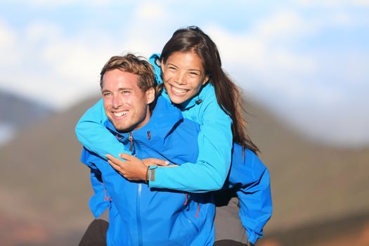 Happy hiking couple piggyback having fun on hike. Fresh young blissful interracial couple. Asian woman hiker and Caucasian man hiker.
