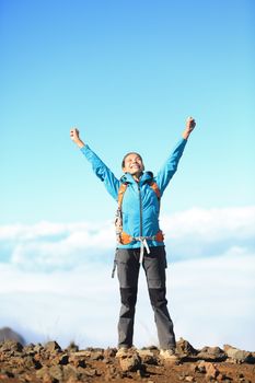 Happy blissful hiker woman in winning / success concept. Hiker woman cheering joyful in bliss with arms raised in the sky after hiking to mountain top summit above the clouds. Asian female model.