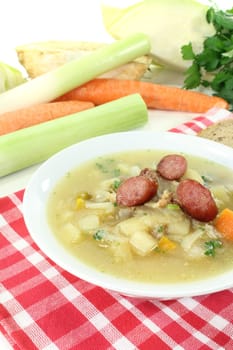 cooked white cabbage soup with vegetables and fried sausage on a bright background
