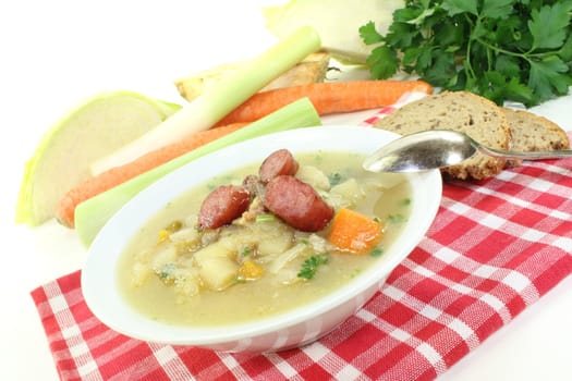 white cabbage soup with vegetables and fried sausage on a light background