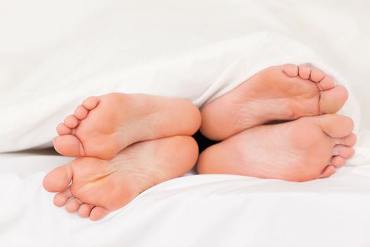Two pair of feet in a bed