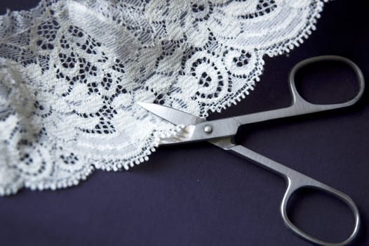 scissors cutting white lace on blue background.