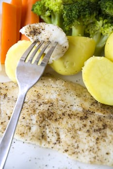 baked fish on fork put on variety vegetables