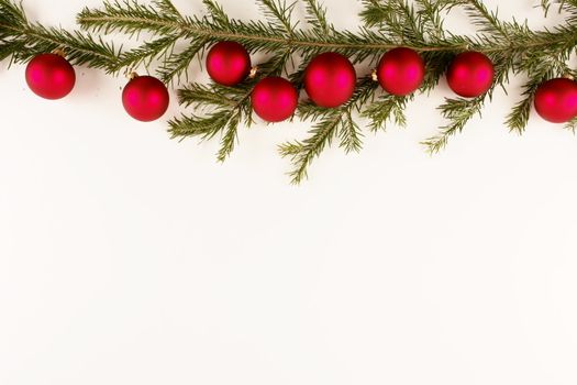 Border of red christmas garland with baubles and ribbons on white.