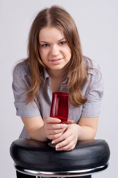 A girl in a bright red T-shirt and a glass sitting on a light background